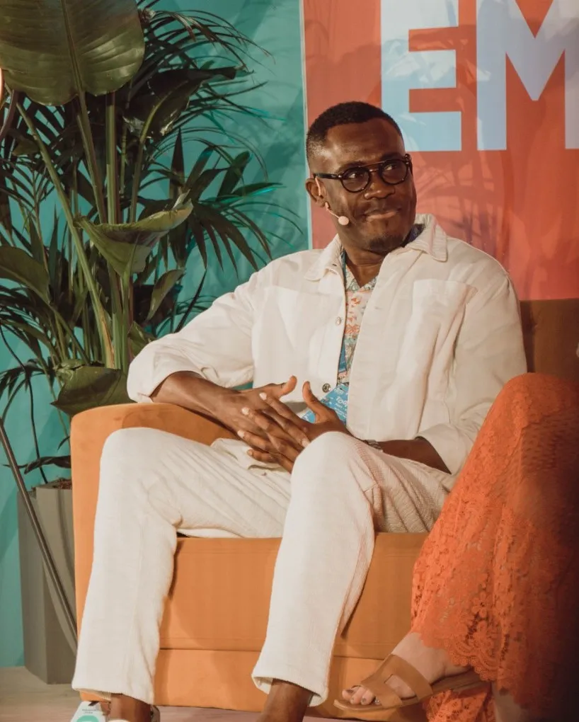 Peter Komolafe smiling on an orange sofa on stage