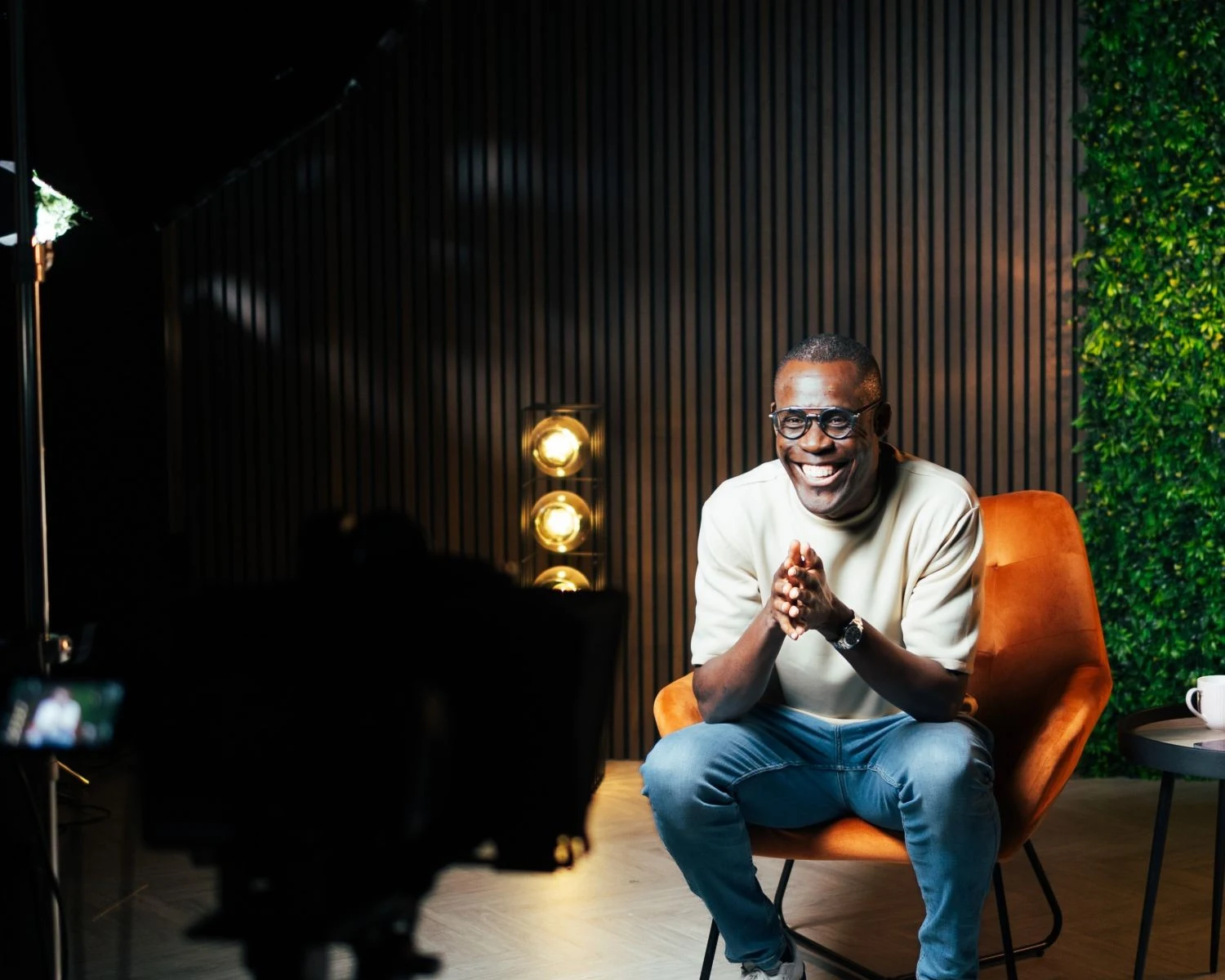 Peter Komolafe smiling in an orange armchair in a studio